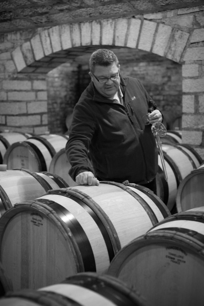 Bertrand de Villaine in the cellar of Domaine de la Romanée-Conti. Notice the stones he has placed on the edge of the barrel; his way of indicating which barrel has been sampled so he can return the wine when the tasting is done. One of many little touches that makes the experience at Domaine de la Romanée-Conti so unique. ©Kevin Day / Opening a Bottle